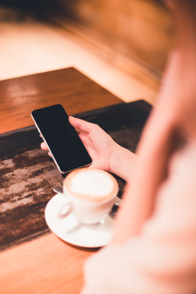 Osoba przy kawie trzyma telefon w ręce, przystępując do kontaktu z prawnikiem prawa spadkowego.